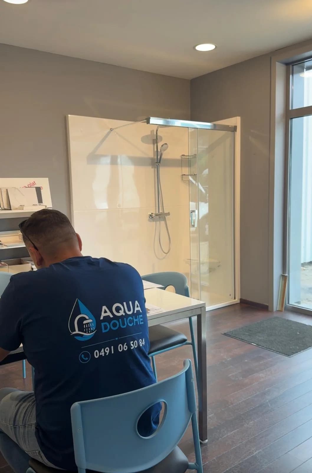 Un membre de l'équipe Aqua Douche dans l'atelier partenaire de Liège, devant une douche de démonstration
